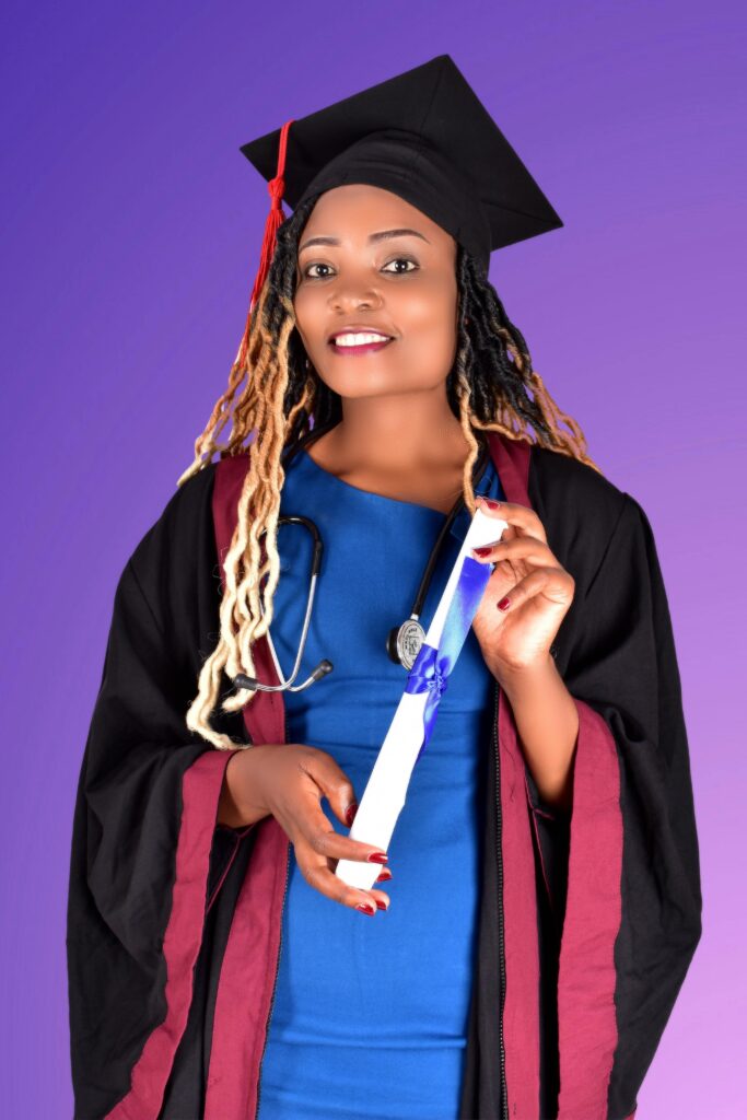 African American graduate in cap and gown, smiling with diploma in studio setting.