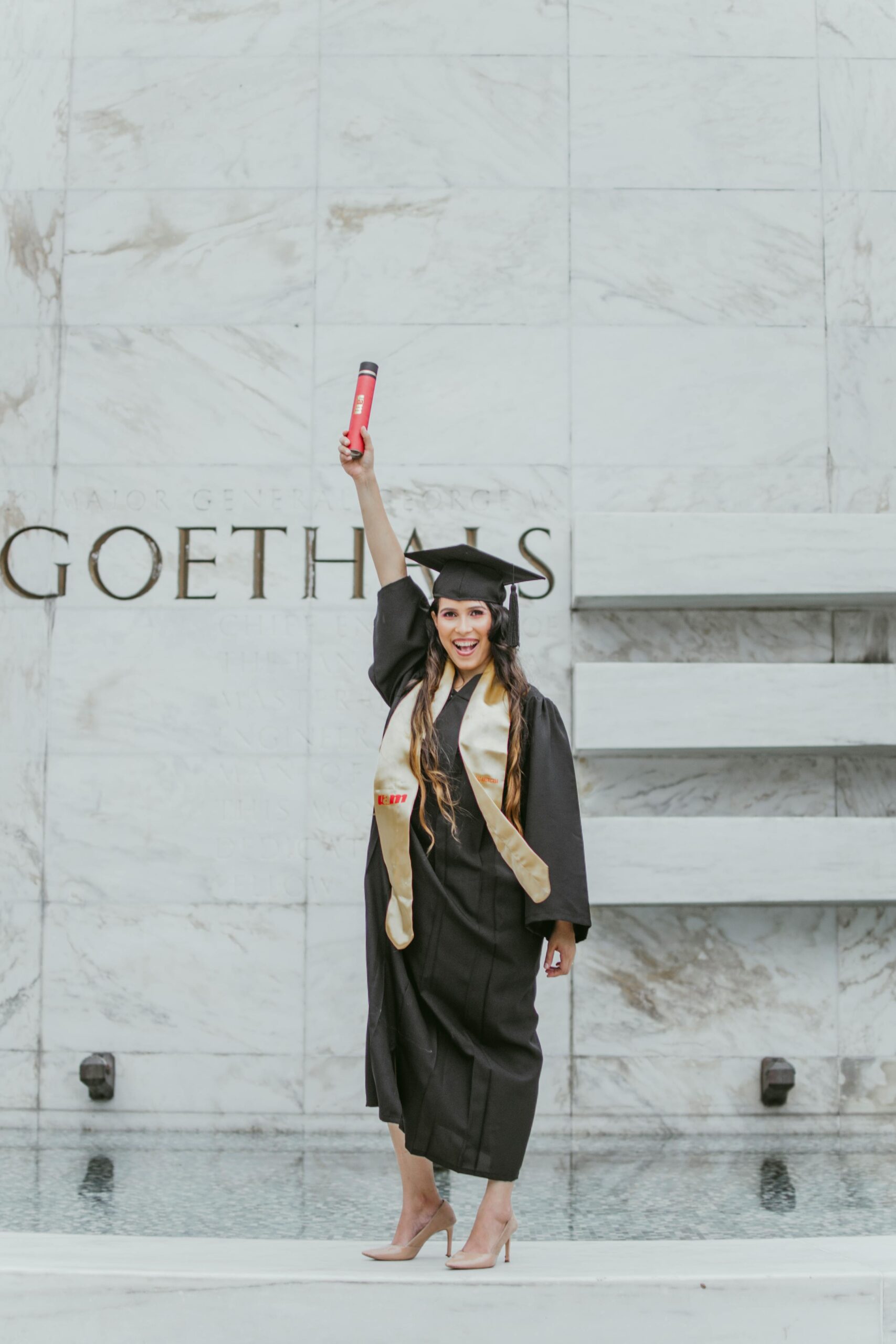Young woman in graduation attire celebrating her achievement at Goethals Monument.